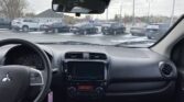 Interior view of a car dashboard and steering wheel, with a snowy parking lot of SUVs visible through the windshield and rearview mirror.