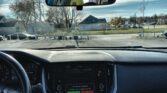 Driver's perspective of a car interior: dashboard and touchscreen with outside street seen through windshield and rearview mirror