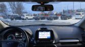 Inside a car looking over the dashboard at a snowy parking lot with several parked SUVs visible through the windshield, winter scene outside.