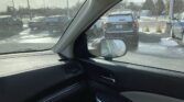 View from inside a car shows a snow-dusted parking lot with other vehicles outside and the side mirror in frame.