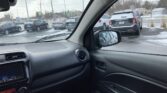 View from inside a car showing a snow-covered parking lot with multiple parked cars, including a black SUV in the foreground and a side mirror in the frame.
