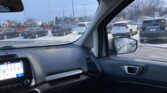View from a car’s driver's seat looking out at a snowy parking lot with several parked SUVs and sedans; the dashboard and touchscreen are in the foreground.