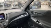 View from inside a car on a rainy day, dashboard and steering wheel in foreground, parking lot with cars outside through a rain-spattered windshield.