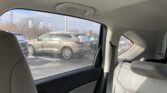 Interior of a car backseat showing beige upholstery, with a parking lot of SUVs visible through the side window on a sunny winter day.