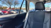 View from the back seat of a car looking out at a car dealership lot with several parked vehicles and leafless trees against a blue sky.