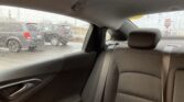 Backseat of a car on a rainy day, with a visible seatbelt and headrest; outside are parked cars through a rain-speckled window.