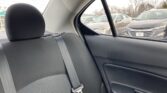 Back seat of a car with a seatbelt fastened, headrest visible, and parked cars seen through the rear window outside.