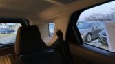 Interior of a car's back seat looking out a side window at a snowy parking lot with parked cars outside.