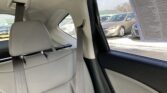 Rear passenger seat in a light gray car with visible seat belts and headrest; outside the window is a parking lot with other cars.