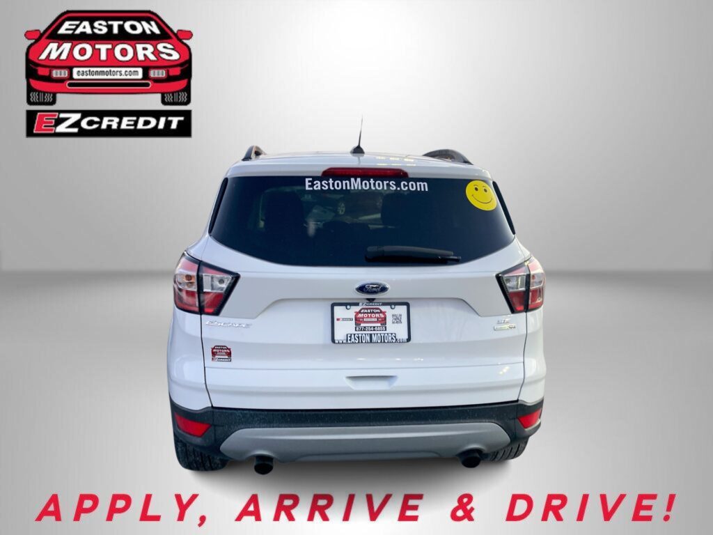 Rear of a white SUV with EastonMotors.com on the rear window, a yellow smiley sticker, and 'APPLY, ARRIVE & DRIVE!' text below