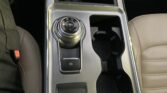 Center console of a car with a rotary gear selector (P, R, N, D) and a glowing orange indicator, plus an electronic parking brake button and cup holders on the right side.