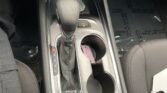 Center car console with automatic gear selector (P R N D L), parking brake button, two cup holders, and a pink tag in the cup holder.