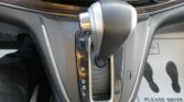 Close-up of a car's center console with an automatic gear selector; the gear indicator shows P R N D S L along the shaft, and the lever is in Park.