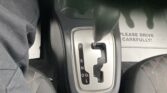Automatic transmission gear selector in a car with P, R, N, D, S, L markings and a floor mat reading 'PLEASE DRIVE CAREFULLY!'