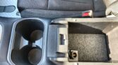 Dark gray car center console featuring two cup holders, a small storage bin, and a red seat belt buckle to the right of the armrest.