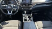 Front interior of a Nissan car showing steering wheel, center touchscreen, and gear shift on a dark dashboard.