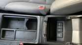 Center console of a car interior with an open storage cubby, a red press seat belt buckle visible between the seats, and control buttons nearby (including a labeled power outlet).