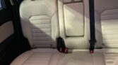 Beige leather car back seat with three seat belts and a central armrest/console.