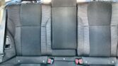 Rear car seat row with three seats, each with woven fabric and visible red seat belt buckles in the center and sides.