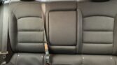 Rear car bench seat with three dark fabric seats and three seat belts, black upholstery and headrests visible at left and right.