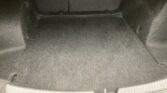 Empty car trunk with dark carpet, back of rear seats visible, small center light, and plastic edge trim along the opening.