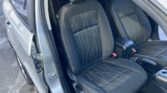 Open car door showing the front seats with black fabric and white stitching; headrests visible.