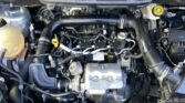 Front view of a car engine bay with hoses, wiring and a yellow-dipstick in the foreground; coolant reservoir visible on the left side under the hood.