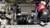 Engine bay of a car with a black plastic air intake box center, red car battery to the right, and various hoses and wiring visible.