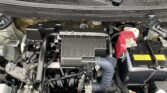 Under-hood view of a car engine bay with the air intake box in the center, battery on the right, and various hoses and wiring visible under a slightly dusty hood surface.