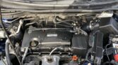 Under-hood view of a car engine with battery, hoses, and air intake; Honda Earth Dreams label visible.