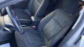 Front interior of a car showing black fabric seats with white stitched geometric pattern, steering wheel on left, and center console visible.