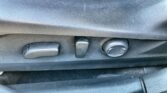 Driver's seat adjustment controls: a small horizontal lever, a larger rectangular lever, and a round knob on a textured panel of the seat side beneath the seatback