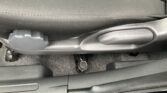 Close-up of a car floor under a seat with a gray fabric seat and a plastic lever on the side; shows the track and floor mat edge.