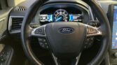 Ford steering wheel close-up with integrated controls and the instrument cluster in the background.