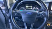 Driver's view of a Ford steering wheel with instrument cluster and digital display visible through the windshield, dashboard in view