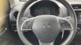 Driver's-seat view of a Mitsubishi interior: steering wheel with controls, analog gauge cluster, and center touchscreen visible behind.