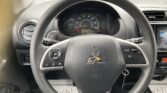 Driver's view of a car dashboard with a circular speedometer behind a textured steering wheel and an infotainment screen to the right.