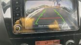 Rearview camera display: parking lot with green guide lines and a red safety line; text says 'Check surroundings for safety'.