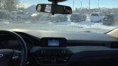 Inside a car on a snowy day, row of parked cars visible through the windshield and rearview mirror.