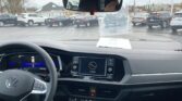 Driver's view of a VW interior: steering wheel, digital dashboard, center console; papers on the dash and a rearview mirror.