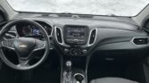 Inside view of a Chevrolet car cabin showing the steering wheel, center touchscreen, and gear shifter with snow outside the windshield