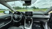 Interior view of a car cabin from the front passenger seat showing the steering wheel, center touchscreen, and gear shifter.