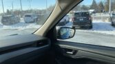 Snowy parking lot seen from inside a car, with other vehicles parked outside and the side mirror in the foreground.