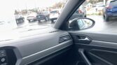 Interior of a car dashboard from the passenger seat, with a view of a parking lot full of cars outside the window and side mirror visible on the right.