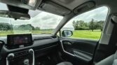 Inside a modern car, view of the dashboard, center console, and sunroof with a grassy field outside through the windows.