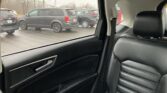 View from the back seat of a car with black leather interior; outside, a dealership lot with gray SUVs.