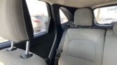 Interior of a car's back seat with two headrests, visible seat belt and grey fabric upholstery, outside parked cars through the windows.
