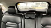 Backseat view of a black leather car interior with headrests, looking toward a rain-speckled rear window showing a street scene outside.