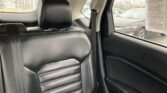 Black leather car rear seat with headrest and visible seatbelt; raindrops on the window outside.