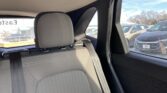 Rear passenger seat in a car with gray fabric upholstery, seatbelt fastened, window view of parked cars outside in a lot.